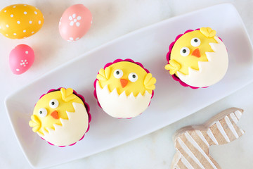 Hatching spring chick cupcakes on a serving plate. Flay lay against a white marble background.