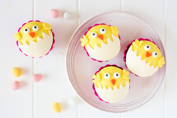 Hatching spring chick cupcakes on a white plate. Flay lay against a white wood background.