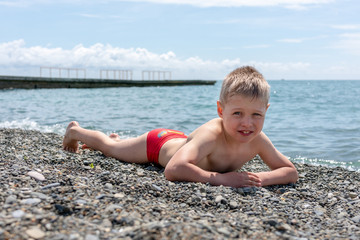 The boy sunbathes on a pebble beach after swimming