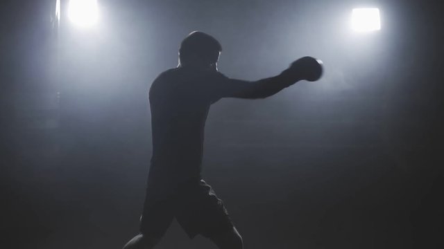 Muay thai fighter punching in smoky studio. Kickboxer training in low light gym in slow motion. Silhouette on dark background