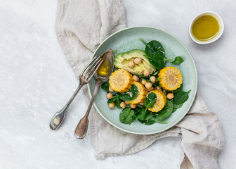 fresh salad bowls with spinach, avocado, chickpeas, sesame and corn with olive oil on marble backround