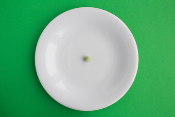 One green pea in the white  plate  on the green background.Top view.Diet minimal concept.