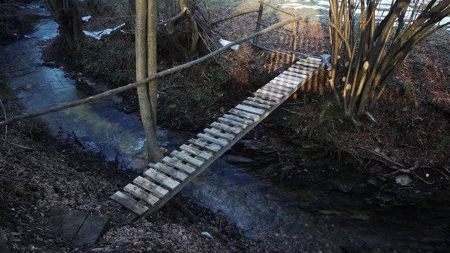 Man crosses creek over wooden bridge - (4K)