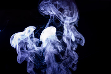 Vape smoke clouds isolated on black background. Hot vape liquid splash in vape coil. Nice aromatic cloud. Low light photo. Underexposed photo in a low key style.