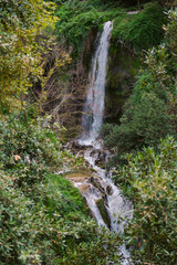 Waterfall among rocks covered with trees and greenery in Gregorain villa in Tivoly