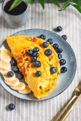 Vegetarian omelette with red and green bell peppers served with banana and fresh blueberry on a table.