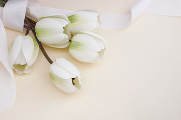 Beautiful fake white tulips with ribbon in pastel background. Concept for Mother's Day celebration with copy space.