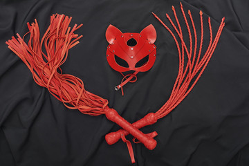 New to BDSM? Top view of red bdsm leather set (whip and mask) on a black silk.