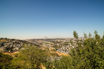 Fototapeta na wymiar Distant view of the cityscape of Old City of Jerusalem with smoke over the mountains and copy space above
