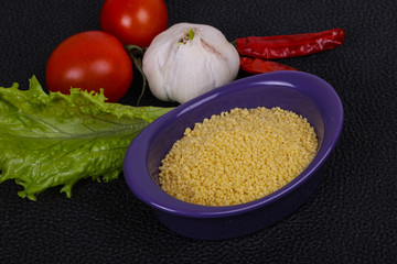 Raw couscous in the bowl served salad leaves, tomato and pepper