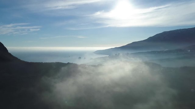 Aerial view of endless ocean, coastline near high mountain in clouds. Shot. Stunning view of a rock in a shadow of the sun, blue ocean, small town down in the valley on cloudy sky background.