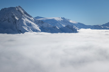 Fototapeta premium Mountain peaks covered in snow above clouds in La Plagne, French Savoy Alps. Winter scenic scenery, blue sky and stunning views.
