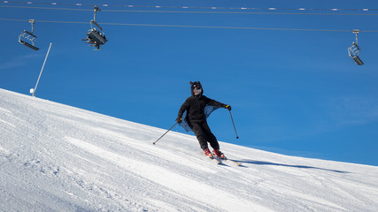 Teenage girl dressed in a bat costume enjoying downhill skiing on a freshly groomed ski slope.