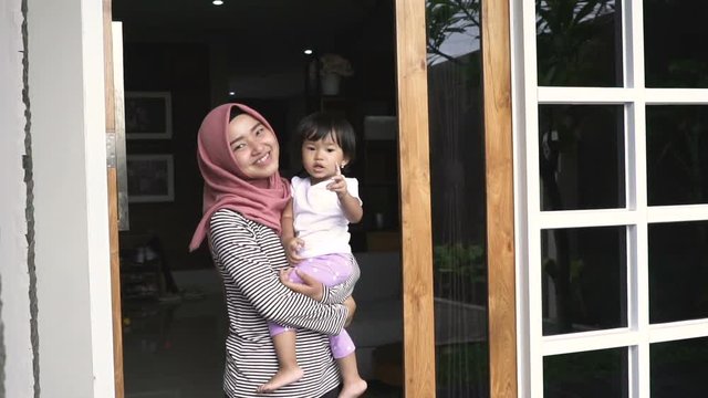 young little baby carry by her mom and wave bye bye in the front door of her house