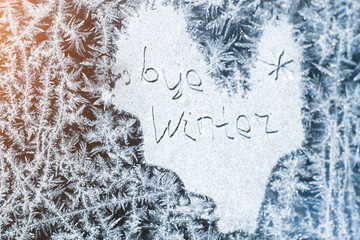 The inscription: goodbye, winter. On a frozen winter window in frosty patterns