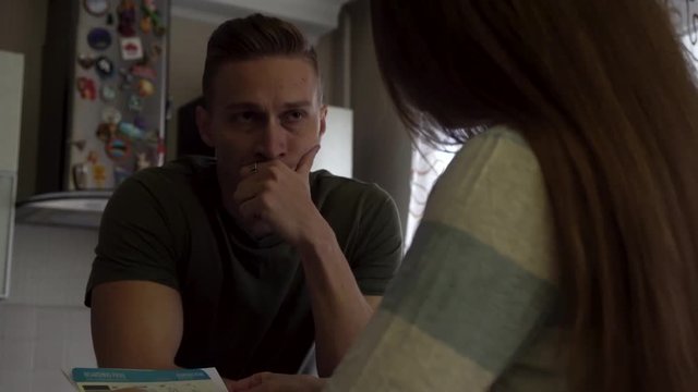 Worried couple reading together a letter standing near the table in the kitchen. Nervous man touching his mouth while his girlfriend opens a letter and begins to read.