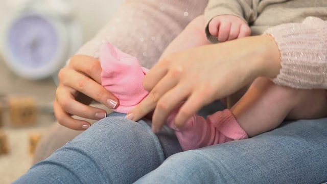 Mother putting on little cute baby girl pink socks, natural clothing materials