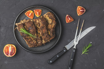 Baked roast pork meat in black ceramic plate, dark concrete surface