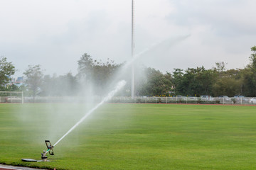 System working on fresh green grass on football or soccer stadium. Sprinkler watering field football. Automatic water irrigation in action. Close-up sprinkler of automatic watering. 