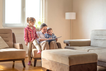 Happy mother with children reading book and enjoying day while spending time together at home