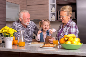 Grandparents with granddaughter preparing pancakes with chocolate cream in the kitchen 