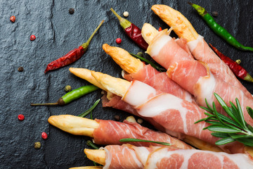 Grissini bread sticks with prosciutto on a black background with rosemary, pepper