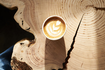 A cup of coffee from above at wooden slab table, top view, sunny cafe.