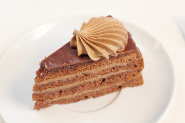 A piece of delicious chocolate birthday layer cake dessert with chocolate cream decoration on a white plate meny style