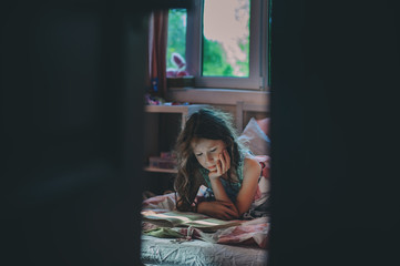 thoughtful kid girl reading book alone in her room in the veening or early morning