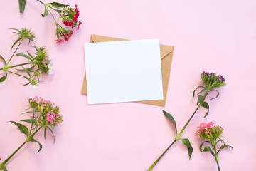 Top view of envelope and blank greeting card with flowers on pink background.