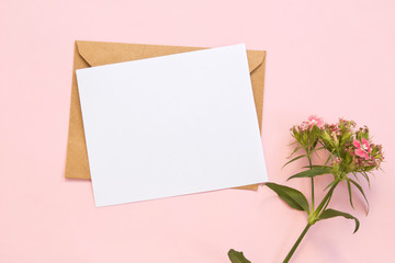 Top view of envelope and blank greeting card with flowers on pink background.