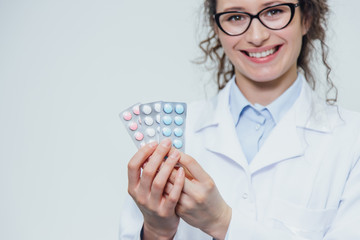 The young doctor's daughter is on a gray background. During this, it holds three blister packs in its hands. Lifting them up sincerely smiles.