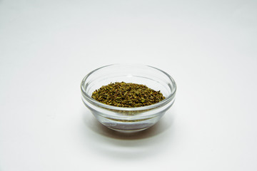 Dried basil in a bowl on a white background. Dried lilac lying on a white table. The concept of using seasonings for dishes. Eating spiced dishes.