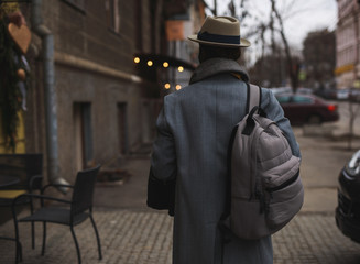 African man in hat walking along city street, back view