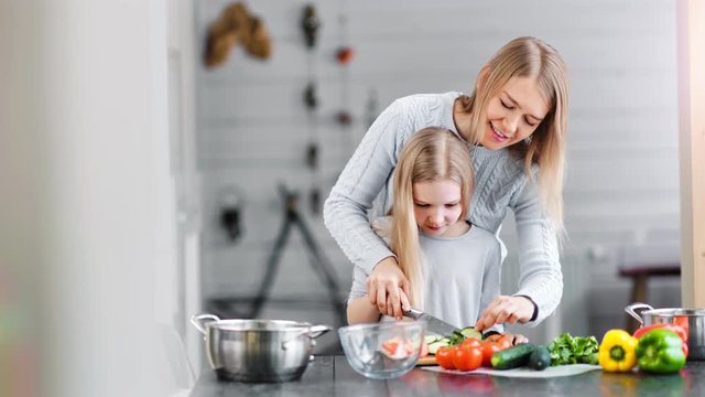 Smiling mother and girl preparing salad in a bowl in a kitchen