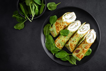 Savory crepes with spinach and feta cheese on black background, top view