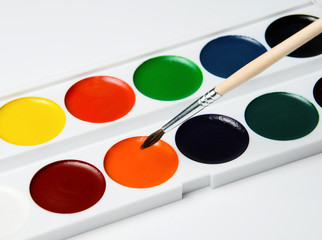 Set of multicolored watercolor paints and brush for drawing. White background. Close-up.