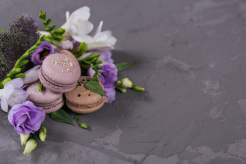Heap of sweet french macaroons mixed with flowers on grey concrete background.