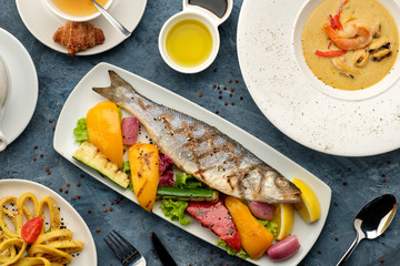 Grilled sea bass with vegetables, seafood soup and fried calamari, top view