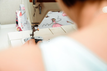Sewing on a sewing machine. Woman uses a sewing machine to sew clothes, decorations from material. Fashion and beauty concept, sewing clothes. A woman works at home, passion.