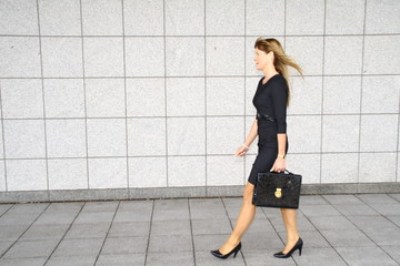 businesswoman with briefcase, walking in front of a wall
