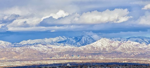 Obraz premium Winter Panoramic view of Snow capped Wasatch Front Rocky Mountains, Great Salt Lake Valley and Cloudscape from the Bacchus Highway. Utah, USA.