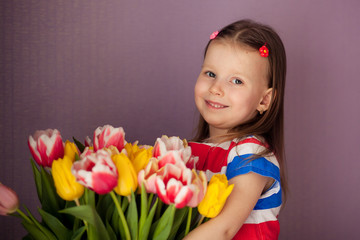 Fototapeta na wymiar Rub a happy cute little girl 3-4 years old, holding a bouquet of tulips. Girl with tulips. Mother's Day, March 8, International Women's Day