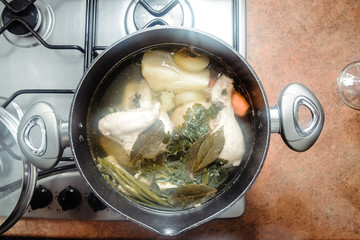 Top view of a pot with broth. View of the boiling soup on the gas stove. The concept of eating and preparing the broth. The soup contains chicken and vegetables.