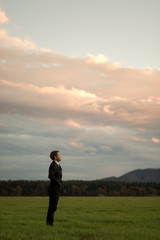 Businessman in a suit standing in green meadow under a glowing evening sky