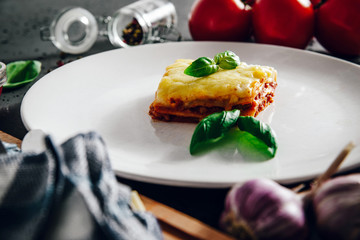 Lasagne on a white plate. On the stone table lies lasagna, spices and food ingredients. The concept of eating and preparing lasagna in tomato sauce.