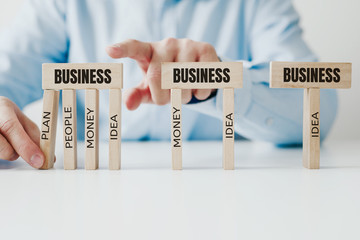 Businessman arranges jigsaw wooden blocks with BIZNES inscription and descriptions of pillars...