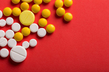 Assorted pharmaceutical medicine pills, tablets and capsules. Red background.
