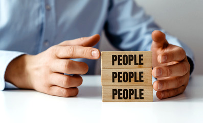 HR concept and human impact on company development. The businessman arranges wooden jigsaw blocks with the word PEOPLE. Personal development, building company's structure, human resource management.