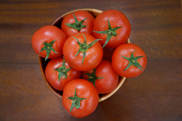 Red tomatoes are in a clay brown bowl on a brown wooden table